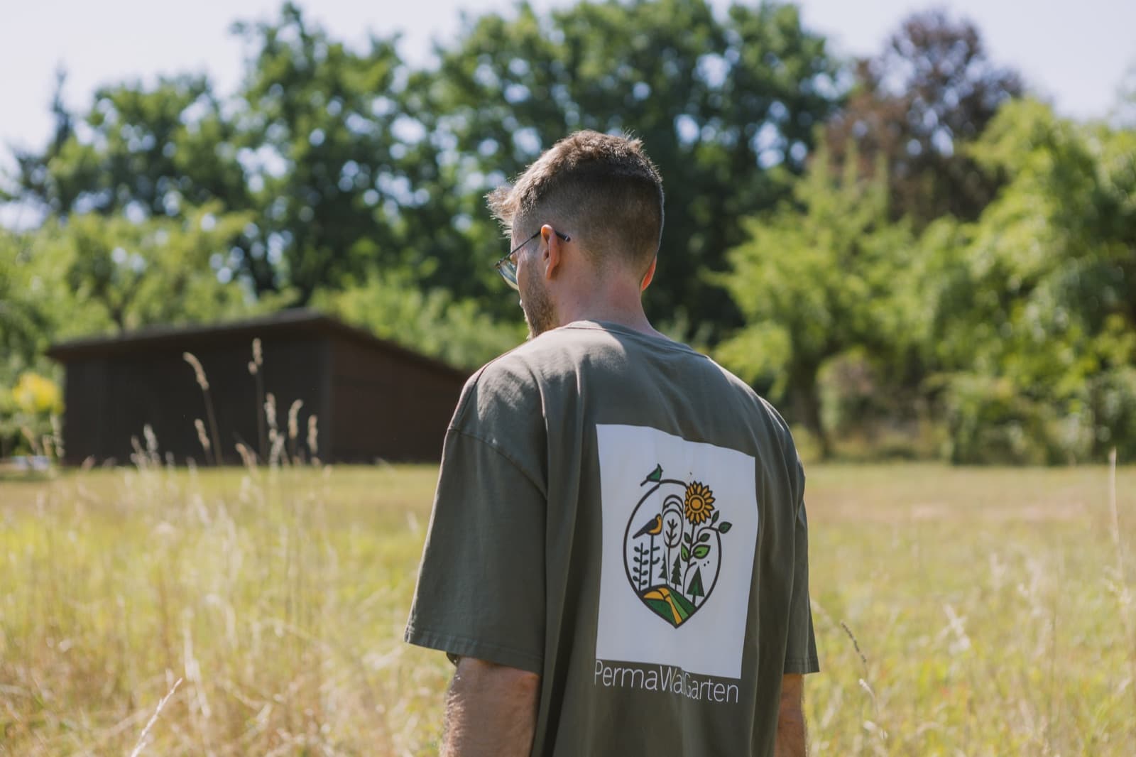 PermaWaldGarten-Logo auf einem T-Shirt, im Hintergrund eine weite Wiese